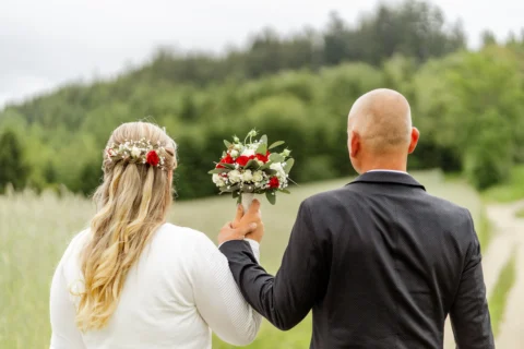 Daniela und Georg heben den Brautstrauß mit roten und weißen Rosen hoch - Martin Schinnerl Fotografie