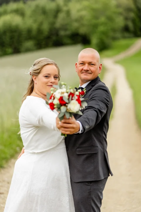 Daniela und Georg strecken gemeinsam den Brautstrauß in Richtung Kamera - Martin Schinnerl Fotografie